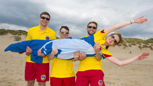 Three male lifeguards holding a female lifeguard in a staged pose for a photographer