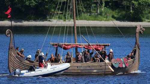 A boat is being filmed on a lake as part of a movie production